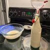 transferring cooked vegan eggnog mixture to glass swing-top bottle